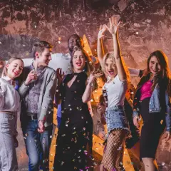 Grupa przyjaciół świętuje w klubie, sypiąc konfetti. Inspiracja, jak się ubrać do klubu: sukienka, jeansy, topy, marynarka.