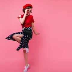 Dziewczyna w stylu pin-up w czerwonej bluzce i spódnicy w grochy tańczy na różowym tle.