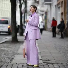 Elegancka kobieta w garniturze w kolorze liliowym, z transparentną torbą, idzie ulicą.