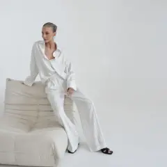 Elegancka kobieta w pasiastym komplecie, uosobienie quiet luxury, siedzi na kremowej sofie.