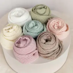 Miękkie kocyki w pastelowych kolorach, każdy z delikatnym wzorem pointelle, ułożone w okrąg.