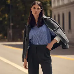 Kobieta w eleganckim stroju, z marynarką narzuconą na ramiona, prezentuje spodnie w odcieniu głębokiego, klasycznego **koloru navy**.