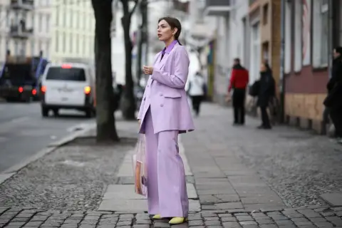 Elegancka kobieta w garniturze w kolorze liliowym, z transparentną torbą, idzie ulicą.