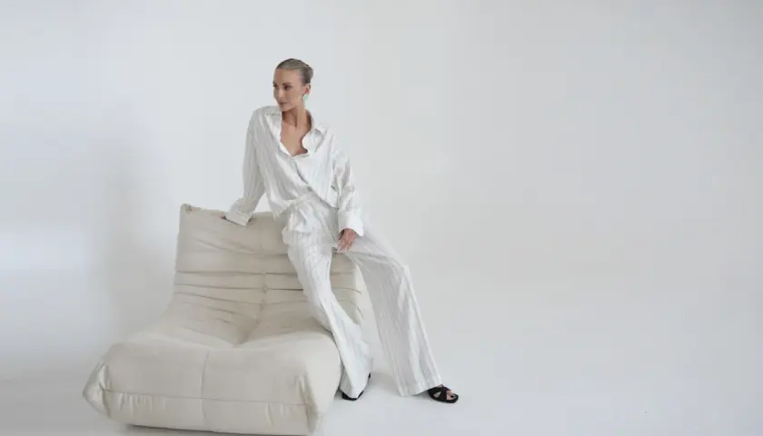 Elegancka kobieta w pasiastym komplecie, uosobienie quiet luxury, siedzi na kremowej sofie.