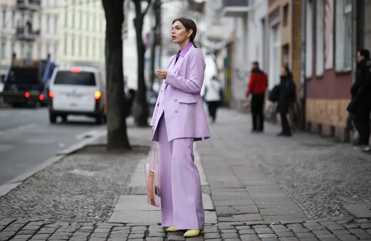 Elegancka kobieta w garniturze w kolorze liliowym, z transparentną torbą, idzie ulicą.