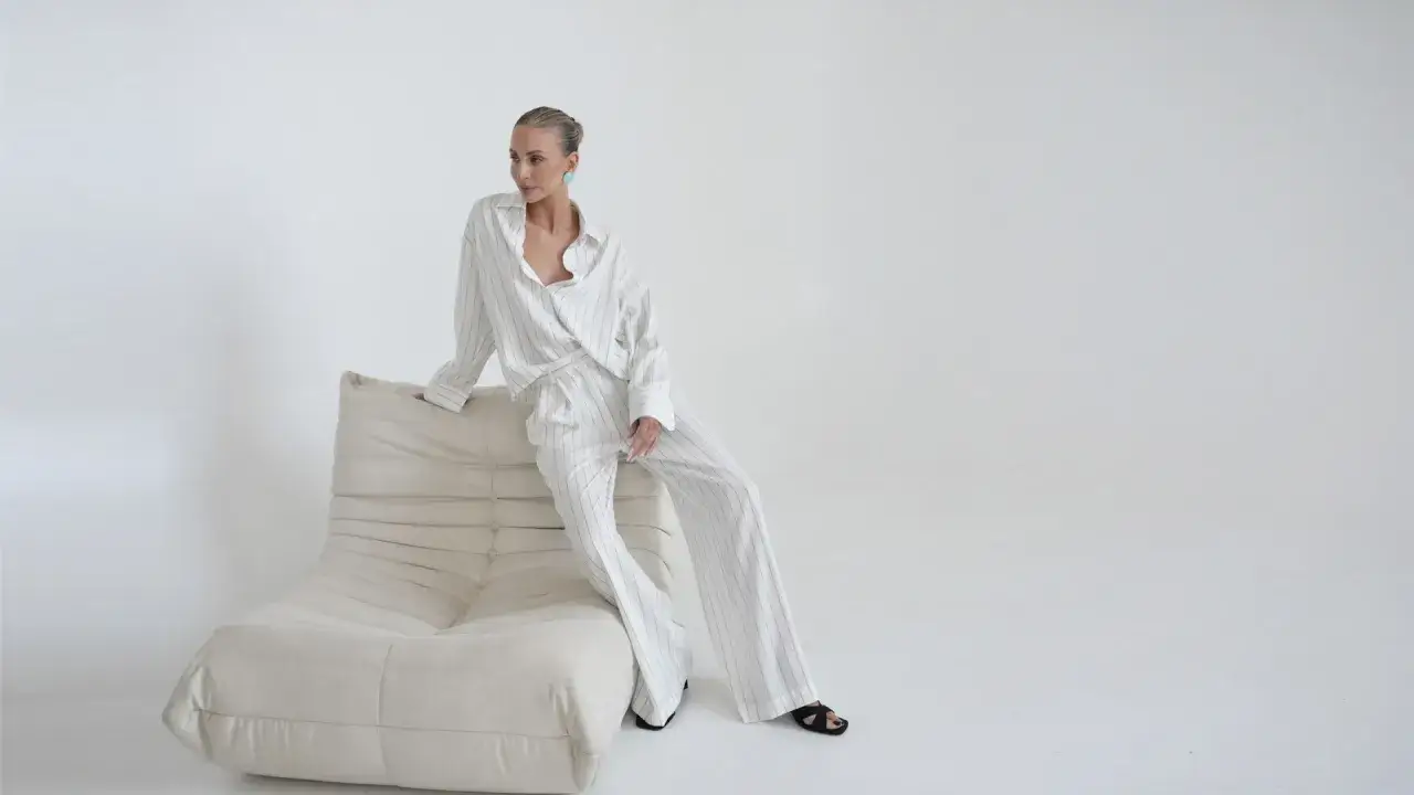 Elegancka kobieta w pasiastym komplecie, uosobienie quiet luxury, siedzi na kremowej sofie.