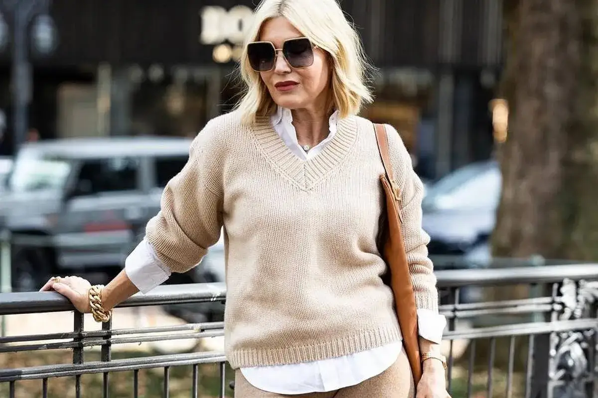 Elegancka kobieta po 50-tce w beżowym swetrze i białej koszuli. Stylowe moda po 50-tce stylizacje.