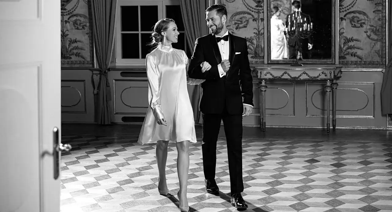 Elegancka para w strojach wieczorowych, idealnych na wyjście do opery. Ona w satynowej sukience, on w smokingu.