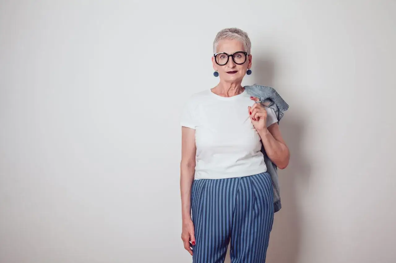 Elegancka kobieta po 50. w okularach i stylowych spodniach w paski. Jej moda to dowód, że wiek to tylko liczba.